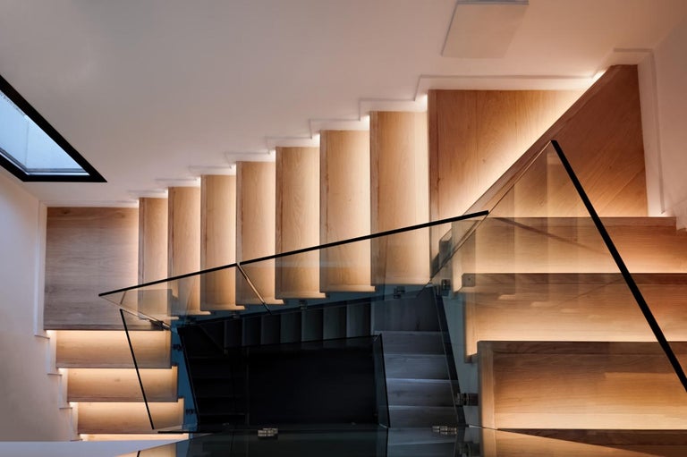 Scară modernă din lemn cu balustradă din sticlă și iluminare LED integrată sub fiecare treaptă.
