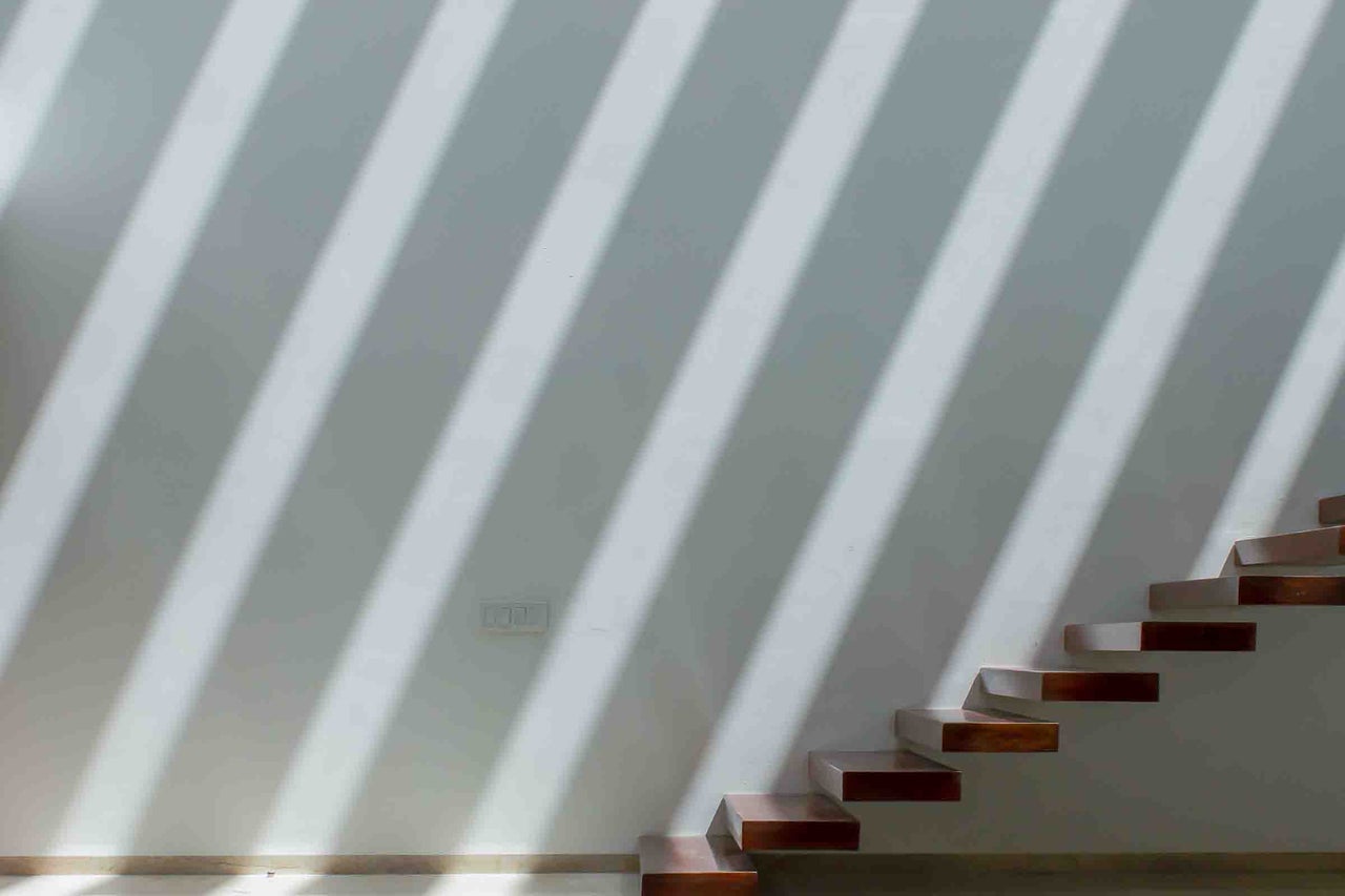 Interior modern cu o scară din lemn minimalistă cu trepte flotante pe un perete cu modele diagonale de lumină și umbră.