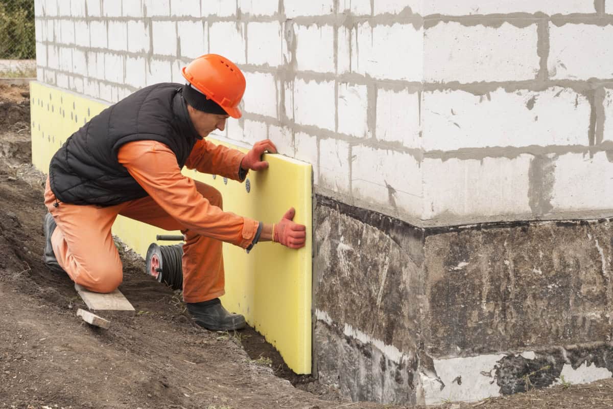Bărbat care fixează izolație perimetrală pe un perete al casei