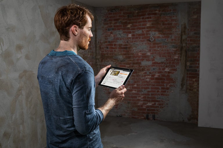 Bărbat cu tabletă într-o cameră brută cu un zid de cărămidă.