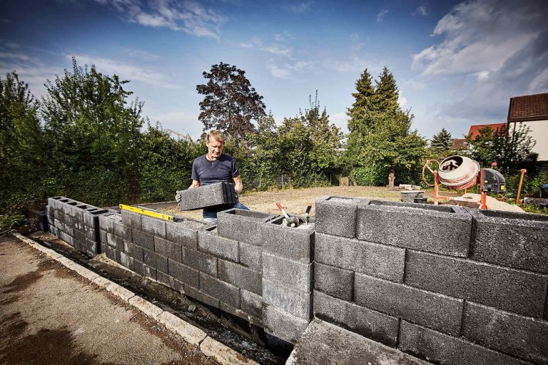 Un bărbat construiește un zid din blocuri de beton în grădină.