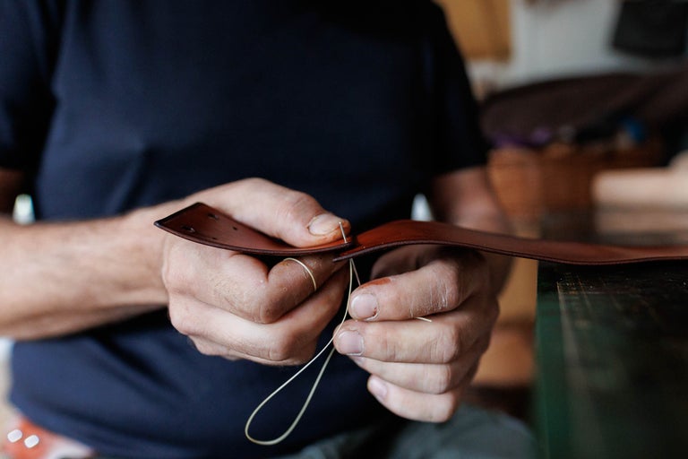 Prim-plan cu un bărbat care coase o bucată de piele cu ac și ață.