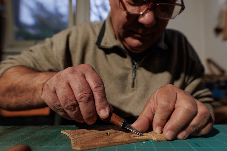 Un bărbat sculptează o bucată de lemn cu o daltă pe o placă de tăiat.