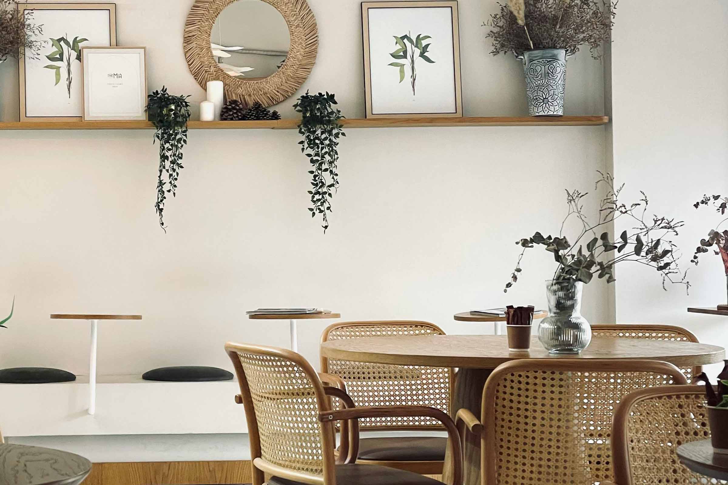 Interiorul unei cafenele cu mese din lemn, scaune din ratan și decorațiuni de perete