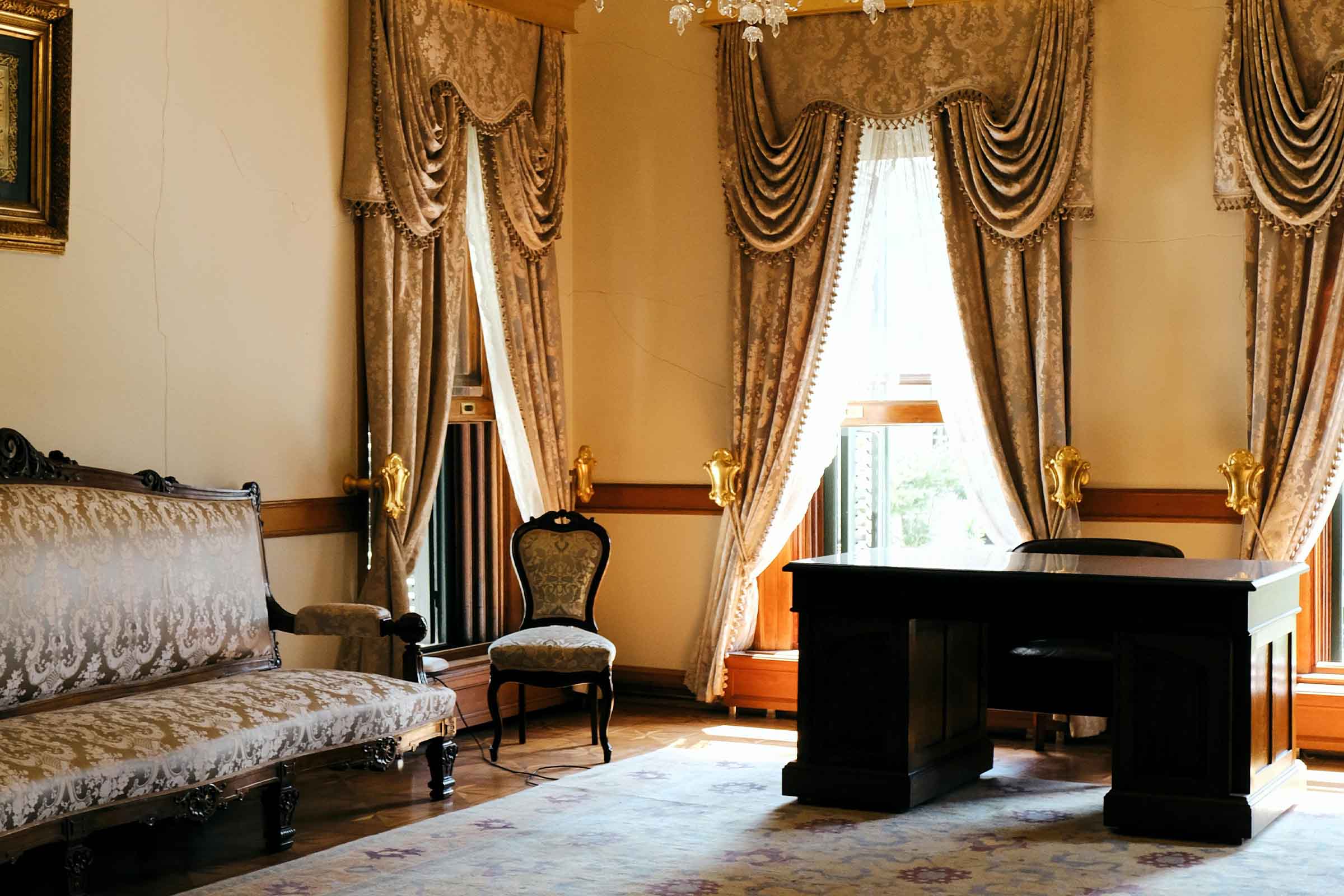 Birou clasic cu birou, fotoliu și canapea sub o fereastră cu perdele