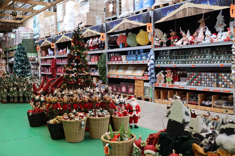 Decorațiuni de Crăciun în magazinul Hornbach cu brazi de Crăciun, figurine și ornamente în rafturi și coșuri.