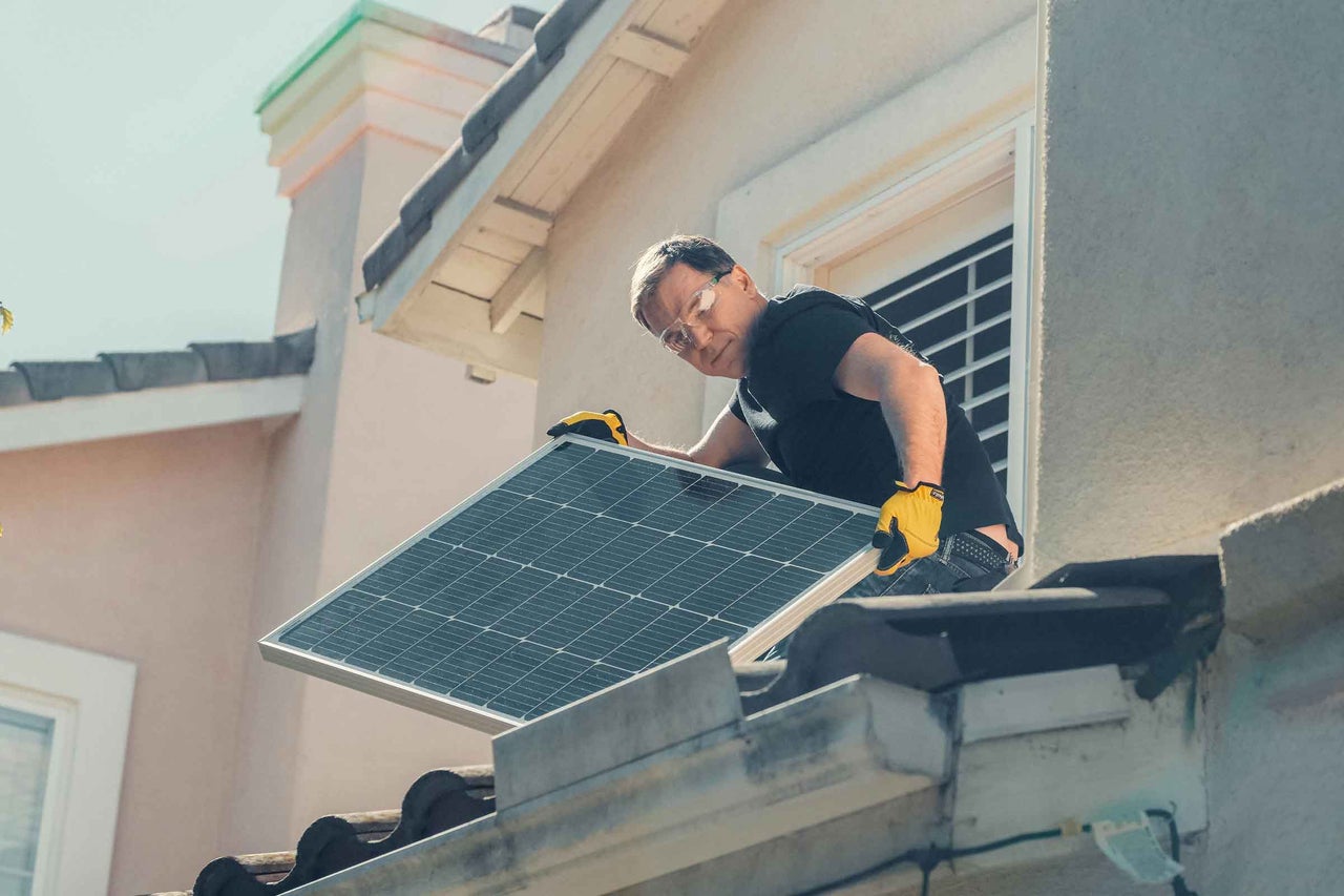 Un bărbat instalează un panou solar pe un acoperiș pentru producerea de energie