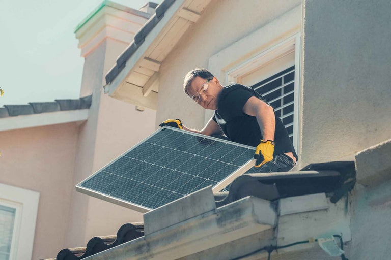 Un bărbat instalează un panou solar pe un acoperiș pentru producerea de energie