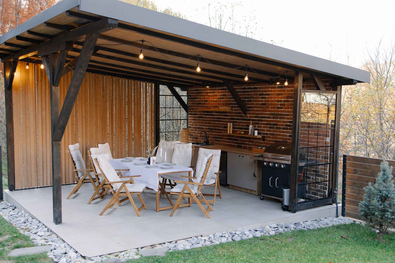 Foișor de grădină cu masă, scaune, grătar și bucătărie de exterior.