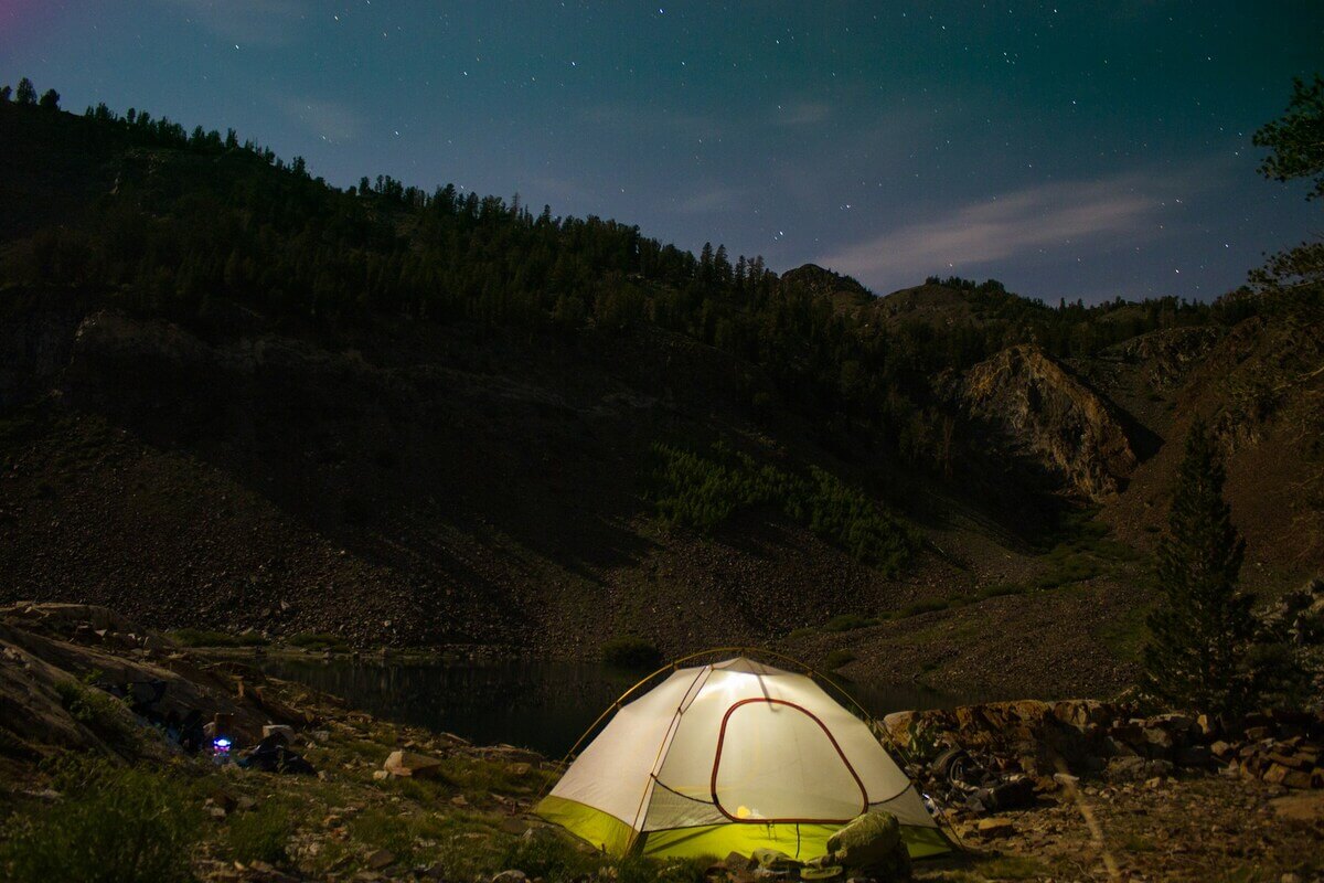 Cort iluminat la camping într-un peisaj montan sub cerul înstelat.