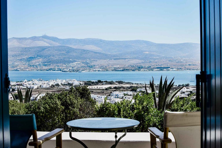 Scenă cu două scaune și o masă pe un balcon cu vedere la mare și la munți