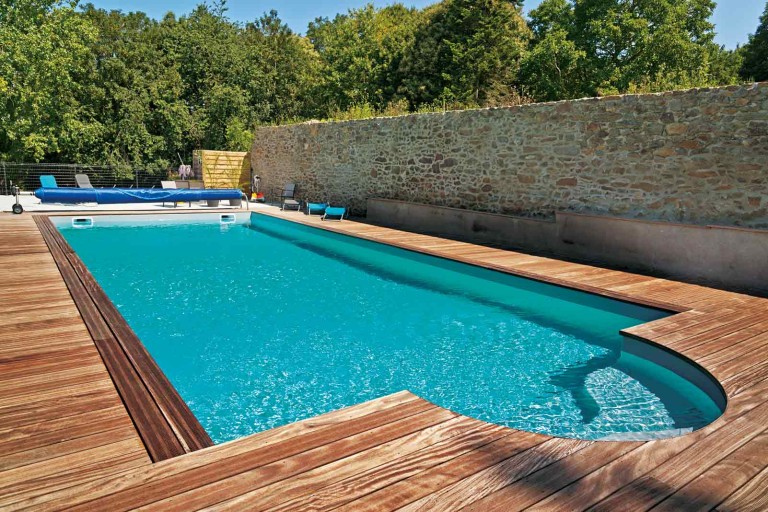 Piscină cu terasă din lemn și zid de piatră în grădină