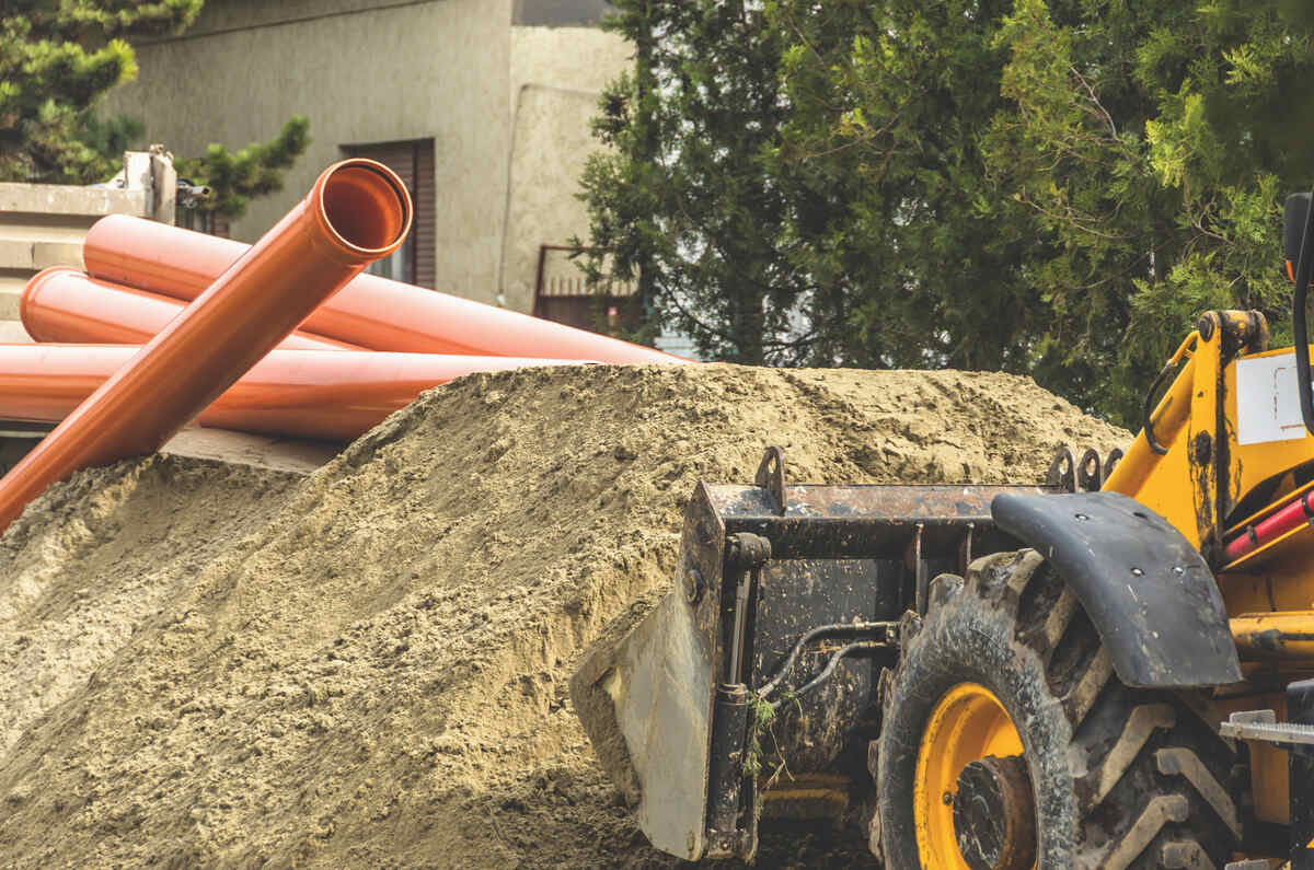 Groapă de construcție cu țevi și un excavator galben