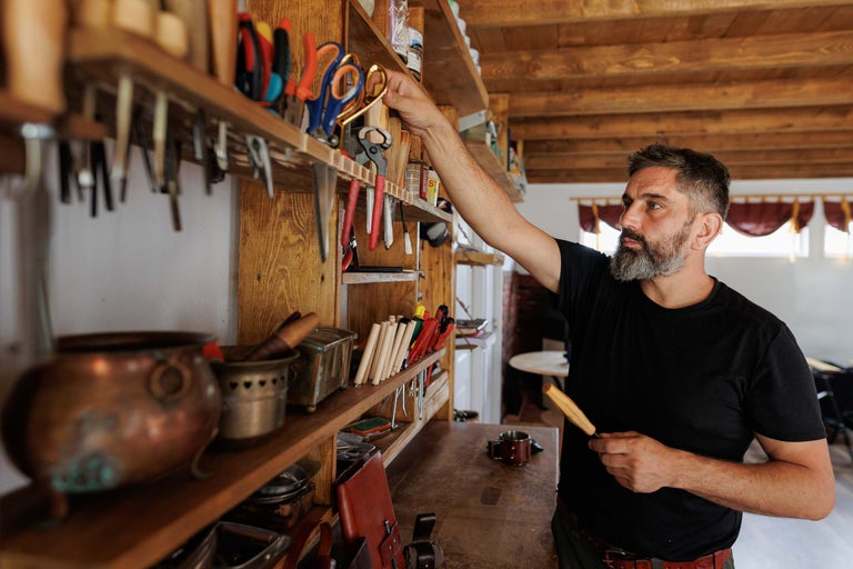 Atelier cu rafturi din lemn, unelte și un bărbat care alege o foarfecă