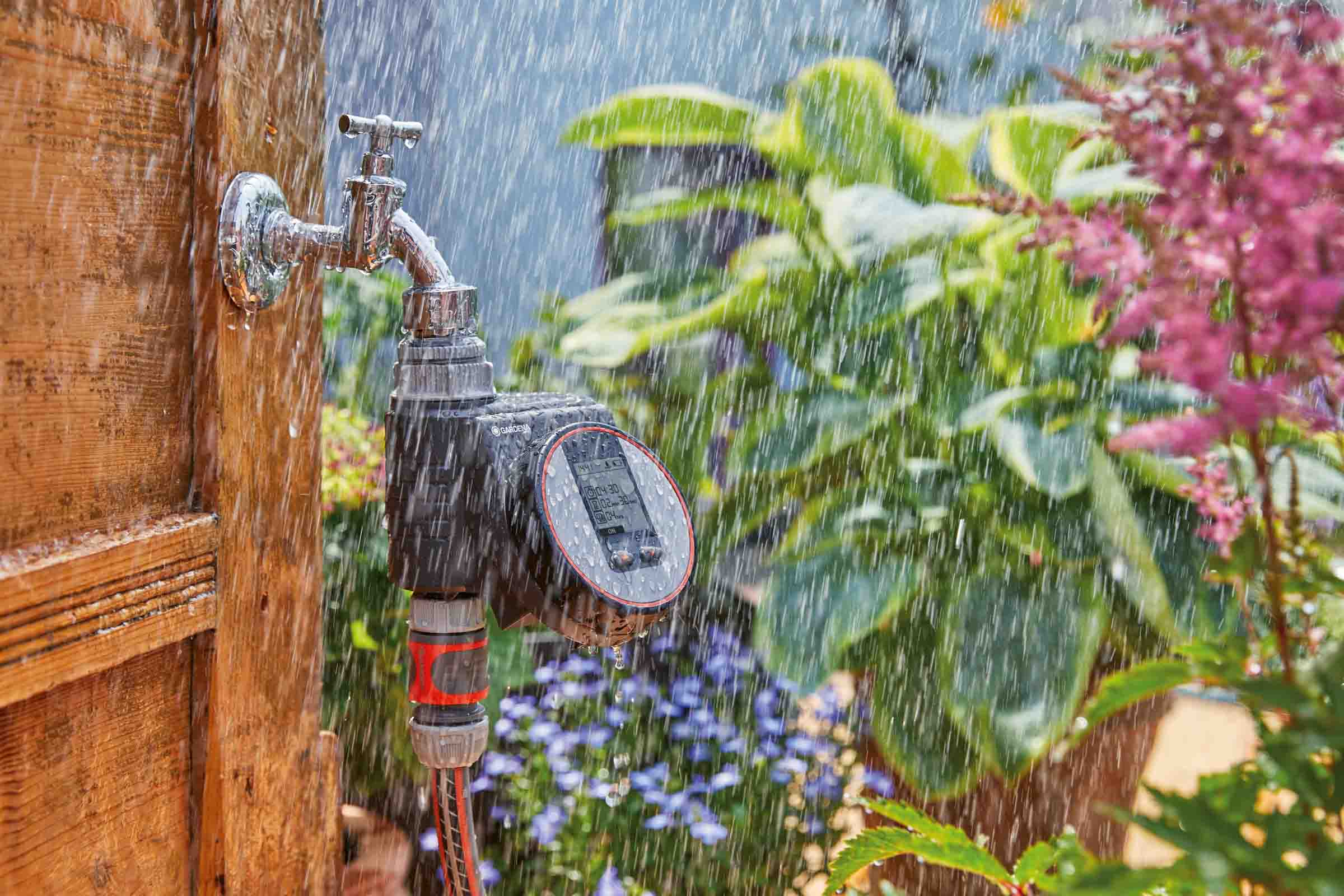 Scenă de grădină cu robinet de apă, calculator de irigare Gardena și plante de grădină sub ploaie.