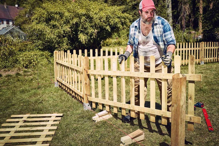 Un bărbat construiește un gard din lemn în grădină.
