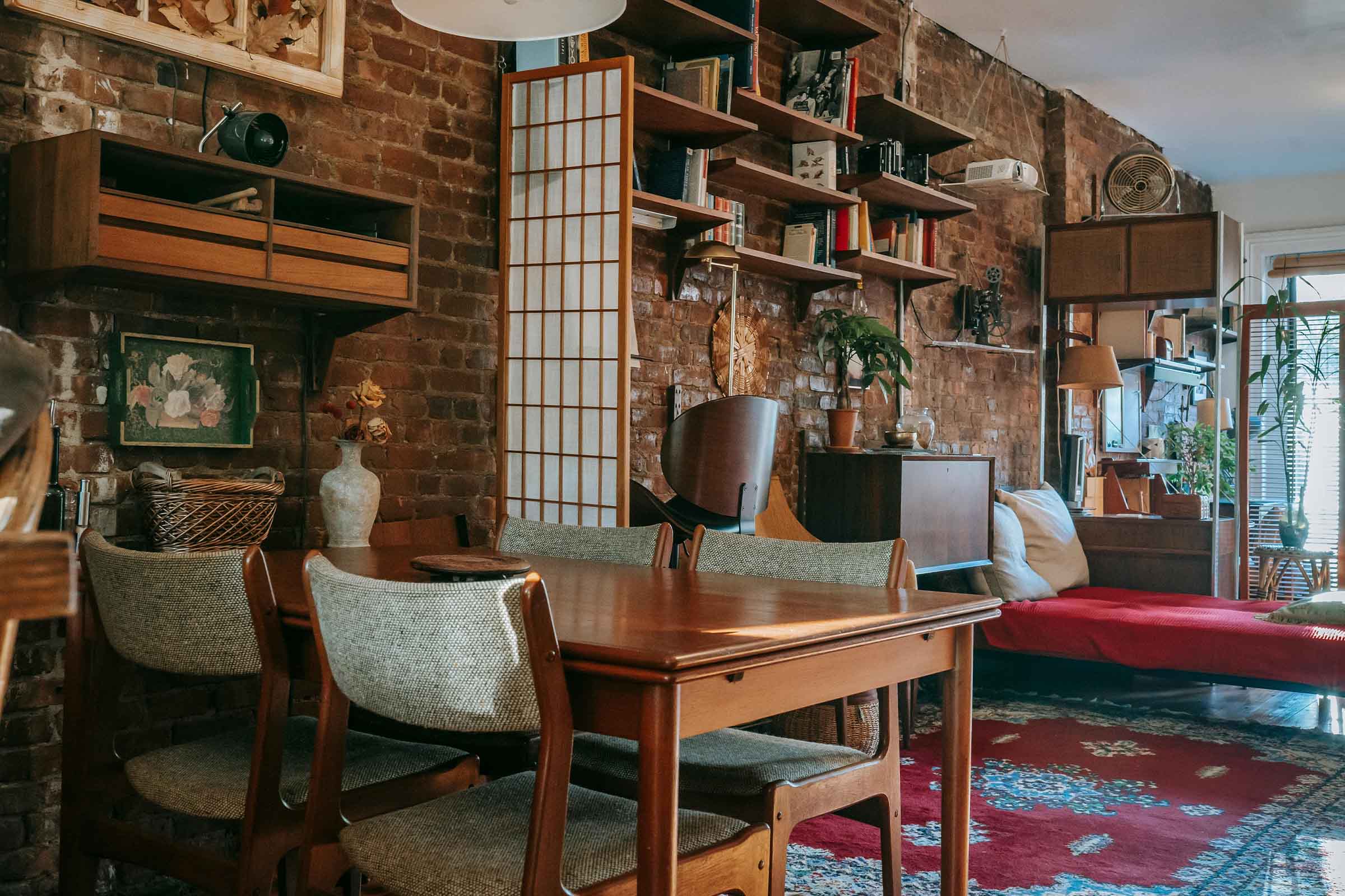 Fotografie de interior a unui living cu perete de cărămidă, masă de sufragerie și biblioteci