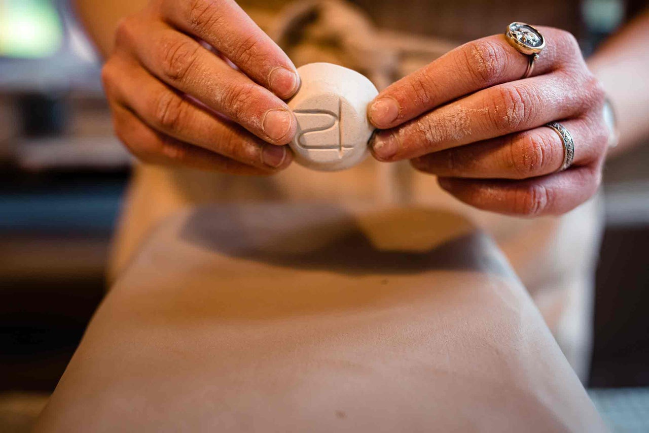 Prim-plan cu mâini care țin o formă ceramică rotundă cu un model imprimat, pentru proiecte de olărit.