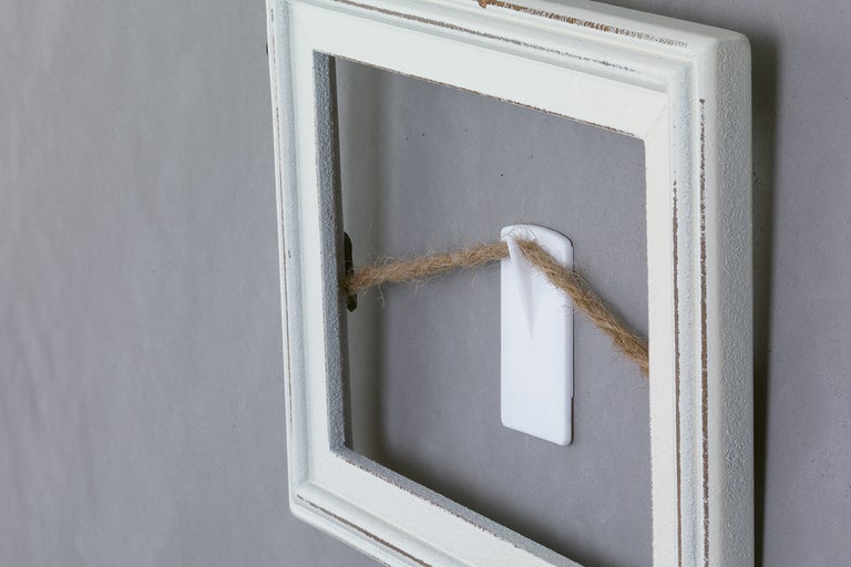 Ramă foto albă cu o sfoară atașată la un cârlig adeziv.