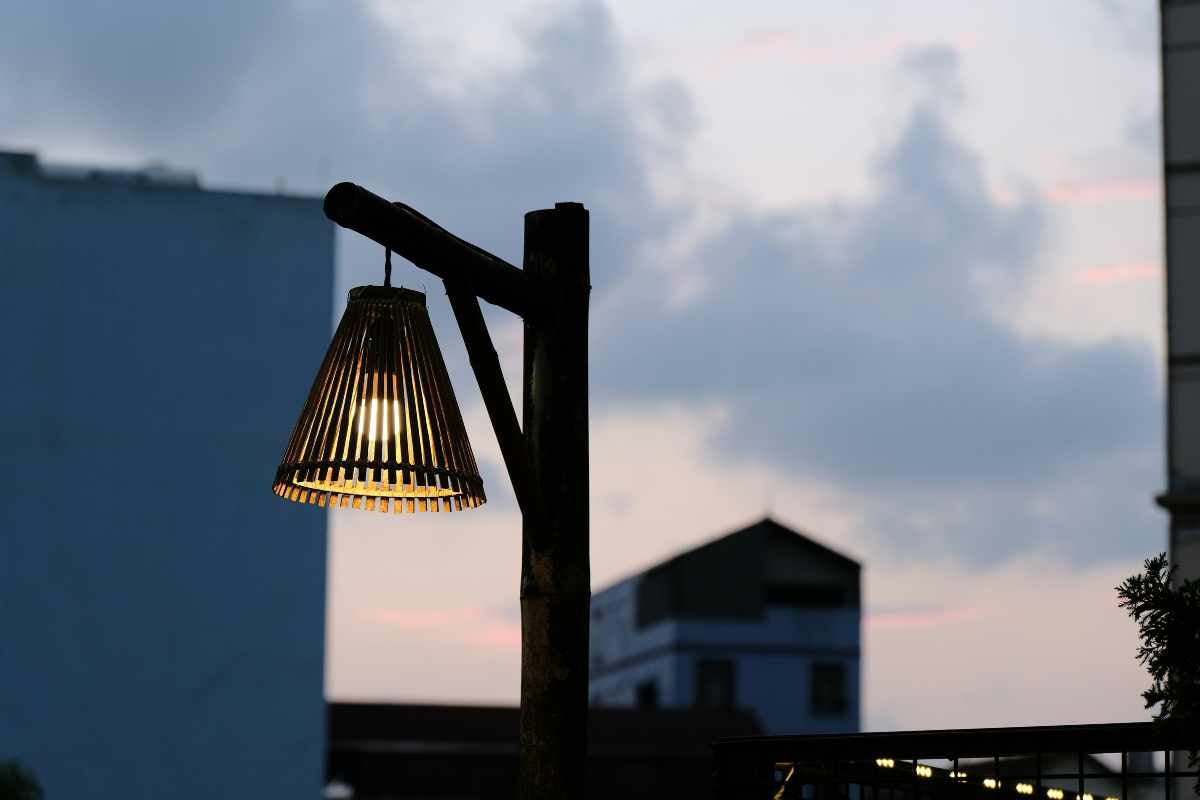 Lampă de grădină rustică din lemn cu abajur conic din bambus pe un stâlp la amurg în exterior.