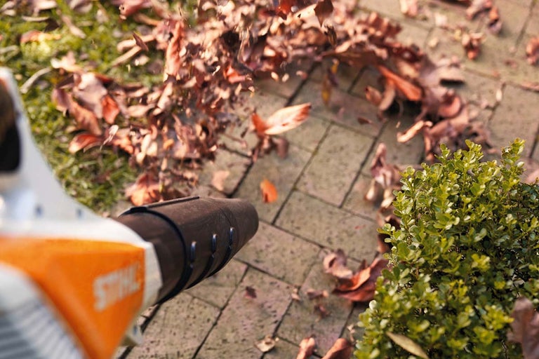 O suflantă de frunze suflă frunzele de pe o potecă de piatră.