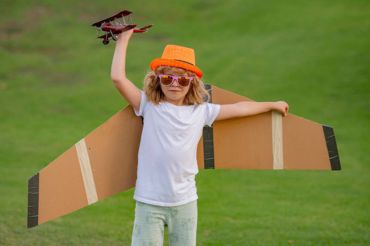 Copil cu avion de jucărie și aripi din carton afară