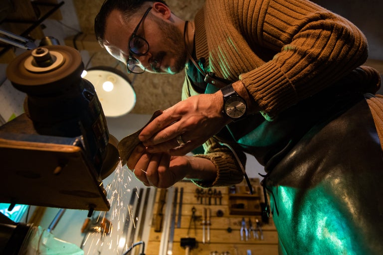 Bărbat șlefuind o bucată de metal cu o mașină de șlefuit într-un atelier.