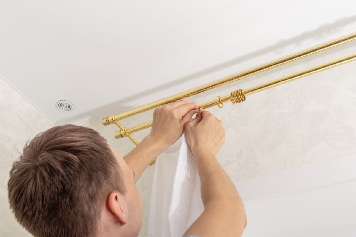 Bărbat care fixează o perdea pe o tijă de perdea aurie