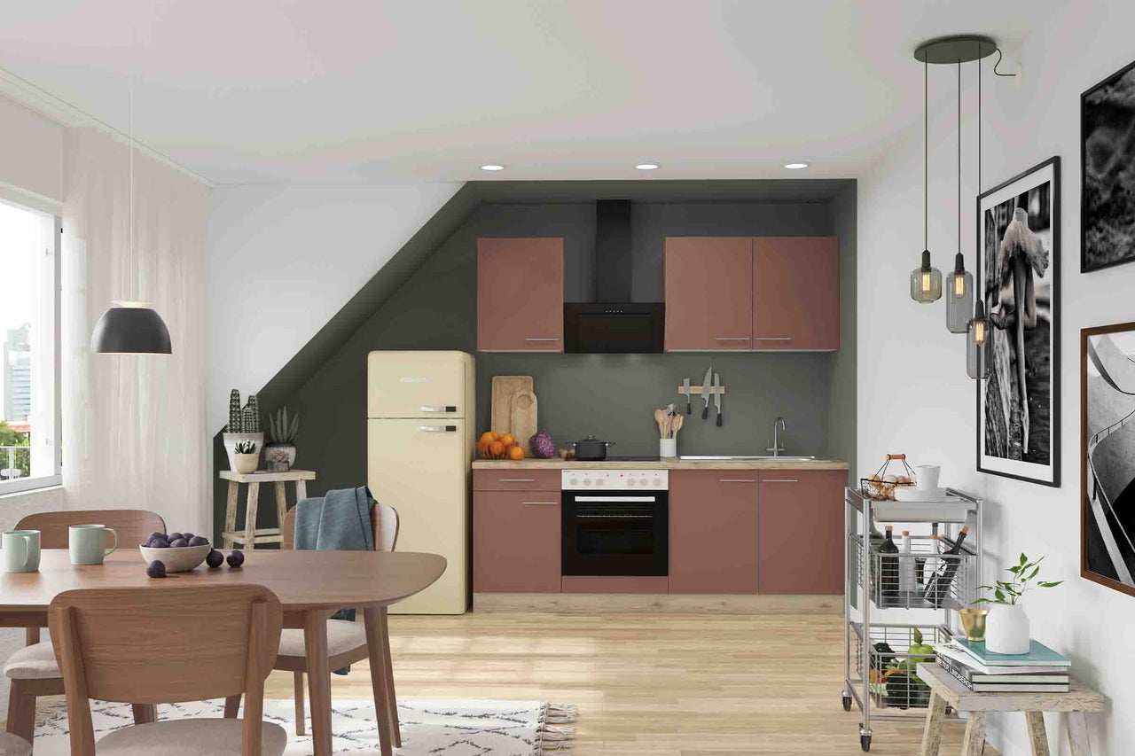 Bucătărie modernă de culoare roz prăfuit, cu electrocasnice negre, frigider retro și zonă de dining într-o cameră luminoasă cu tavan înclinat.