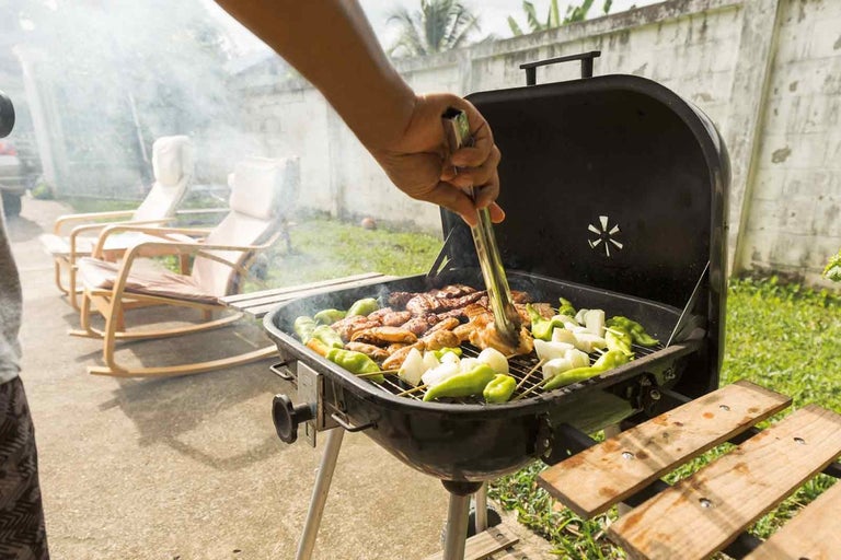 Grătar de exterior cu carne, ceapă și ardei, manevrat cu clește pentru grătar.