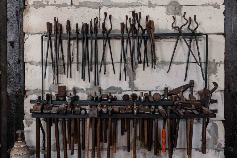 Pe perete sunt atârnate diverse clești de forjă și ciocane pe un raft.