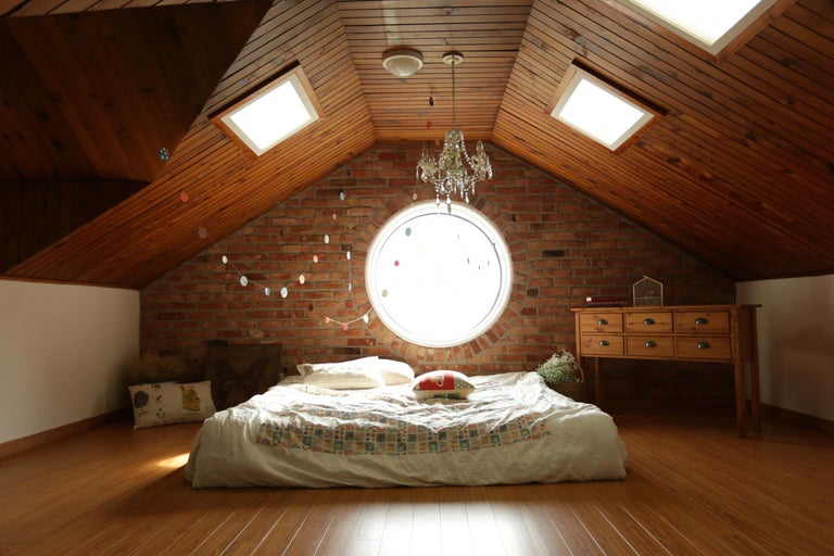Cameră de mansardă cu perete de cărămidă, pat și mobilier din lemn