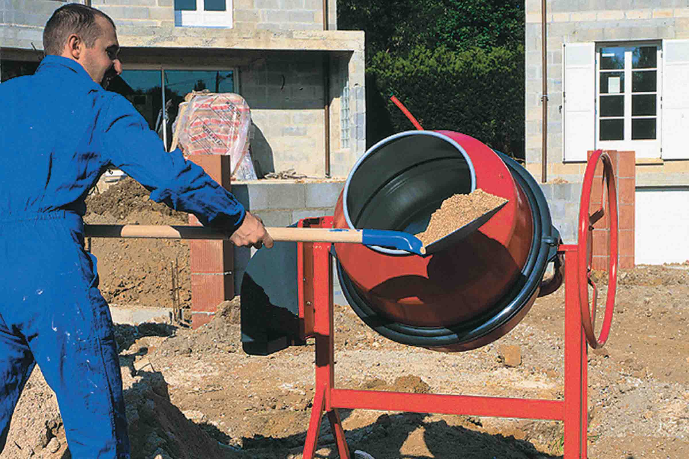 Un bărbat umple un mixer de beton cu o lopată pe un șantier.