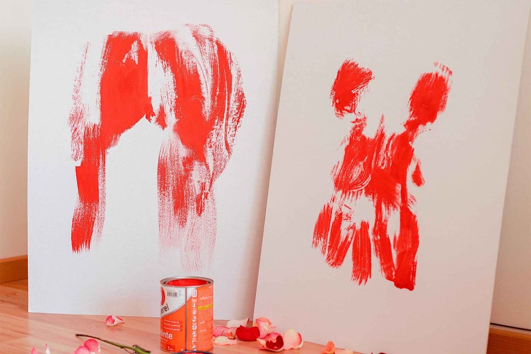 Două pânze albe cu modele abstracte de vopsea și un recipient cu vopsea pe o podea de lemn