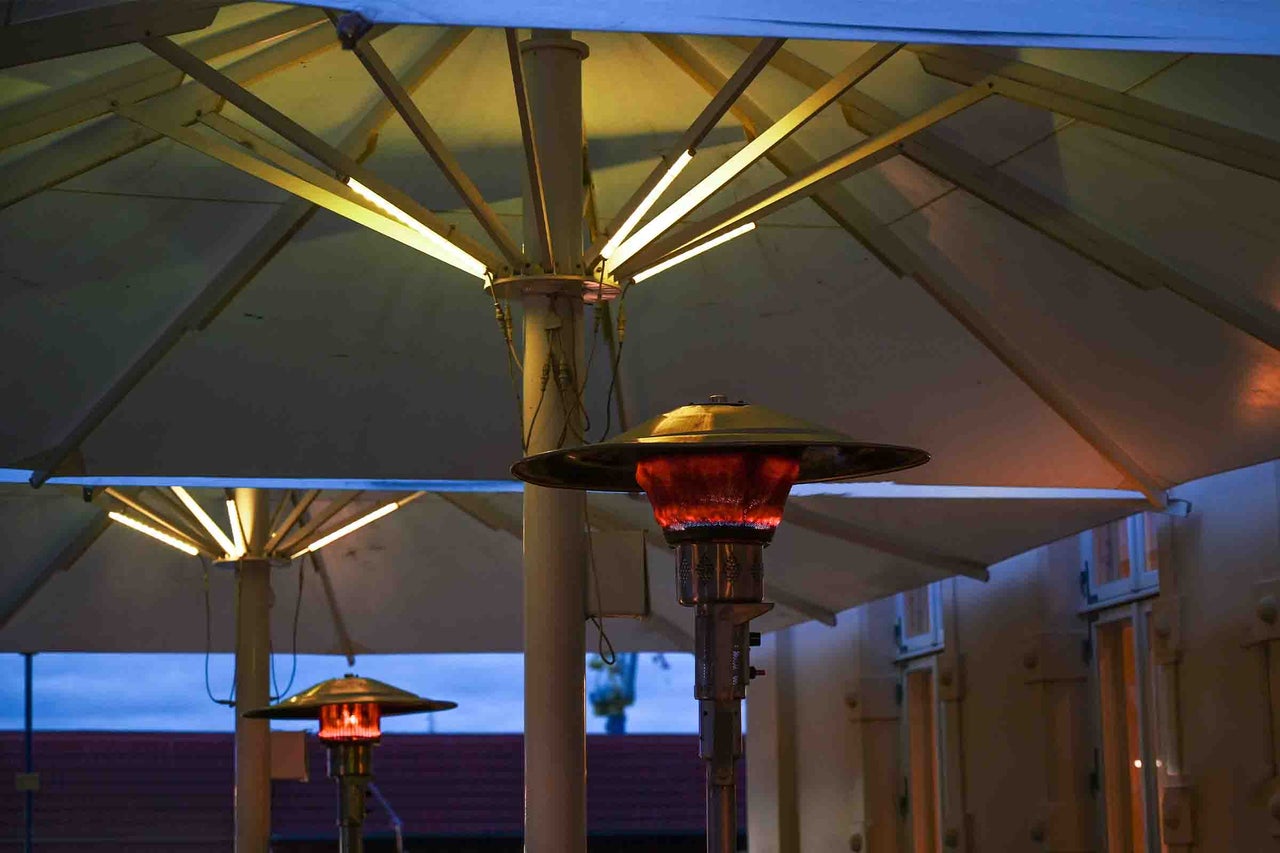 Încălzitor de terasă pe gaz sub o umbrelă cu iluminare LED integrată pe o terasă.