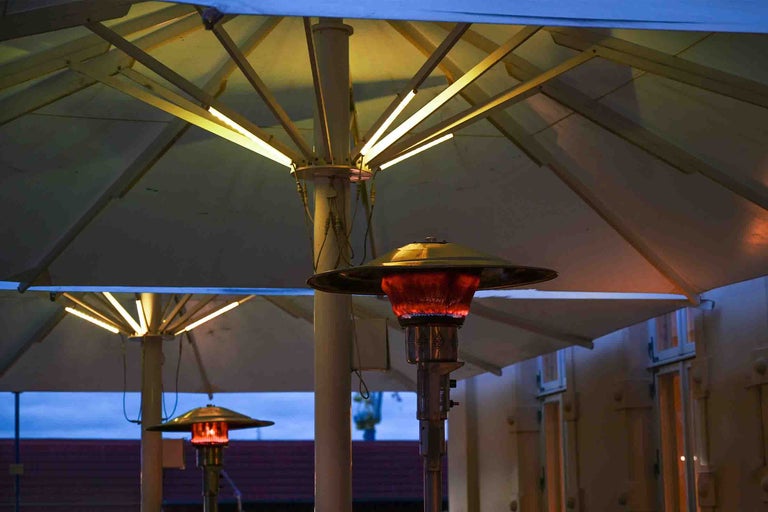 Încălzitor de terasă pe gaz sub o umbrelă cu iluminare LED integrată pe o terasă.