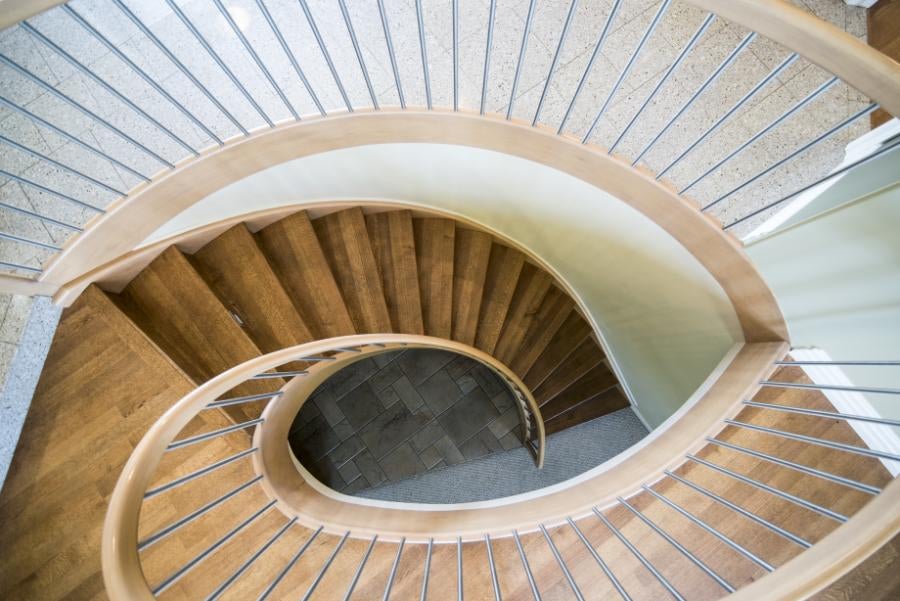 Vedere de sus a unei scări în spirală din lemn, cu o balustradă din tije metalice și o mână curentă din lemn.