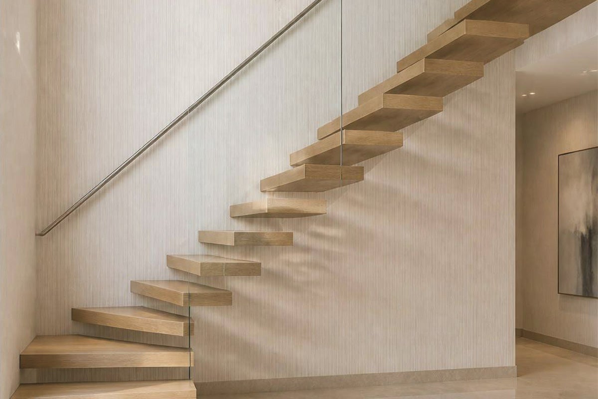 Scara modernă din lemn în consolă cu balustradă din sticlă și mână curentă montată pe perete într-un interior luminos.