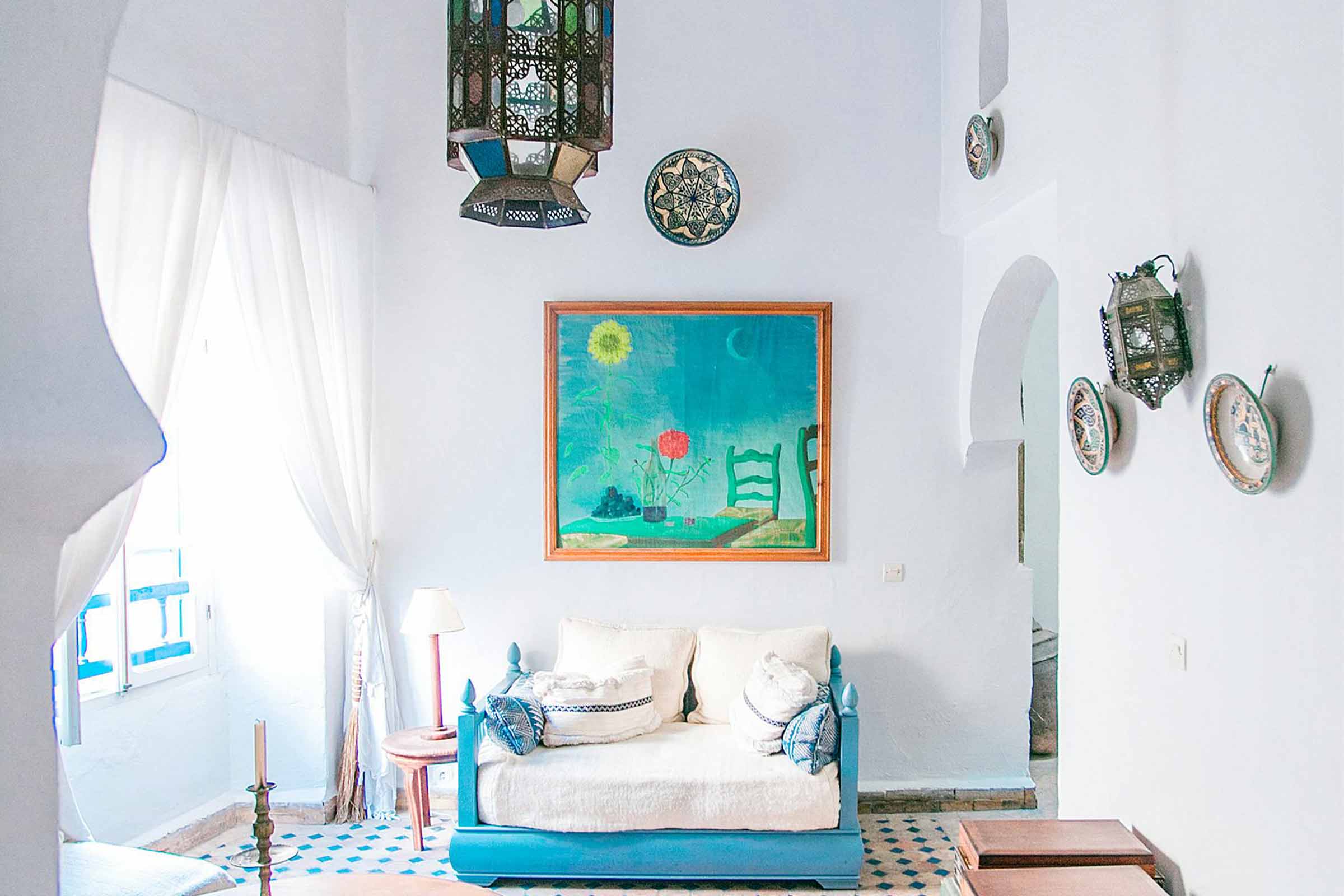 Cameră de zi luminoasă în stil marocan cu canapea albastră, gresie cu model și lămpi decorative