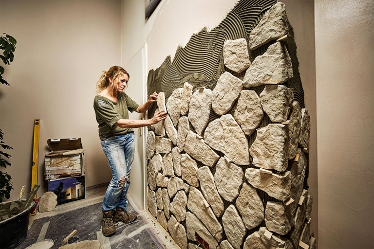 Femeie montând placaje de piatră pe un perete interior.