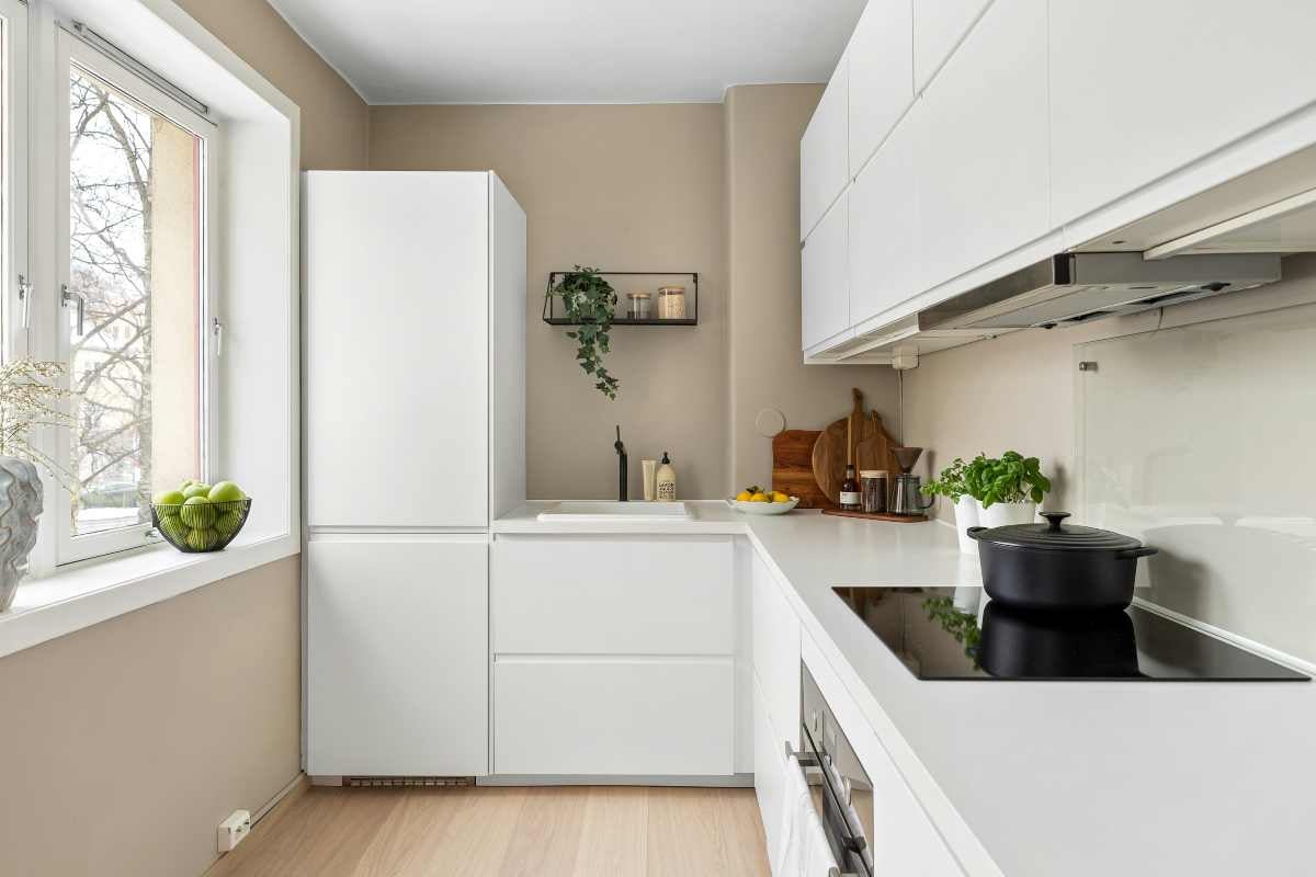 Bucătărie modernă și luminoasă cu dulapuri albe fără mânere, blat alb și electrocasnice încorporate inclusiv plită cu inducție și chiuvetă.