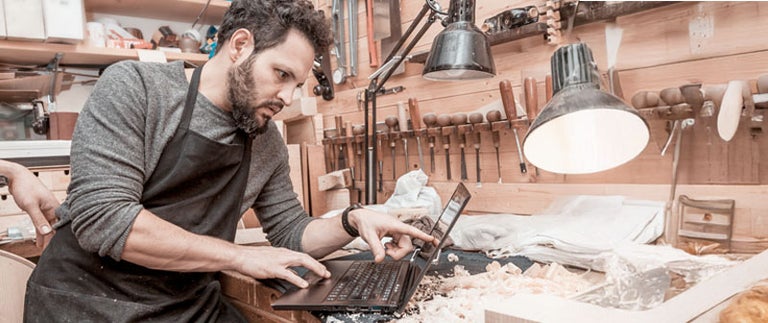 Un meșter lucrează cu un laptop într-un atelier.