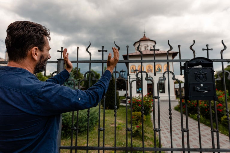 Bărbat stând în fața unui gard cu simboluri religioase uitându-se la o biserică