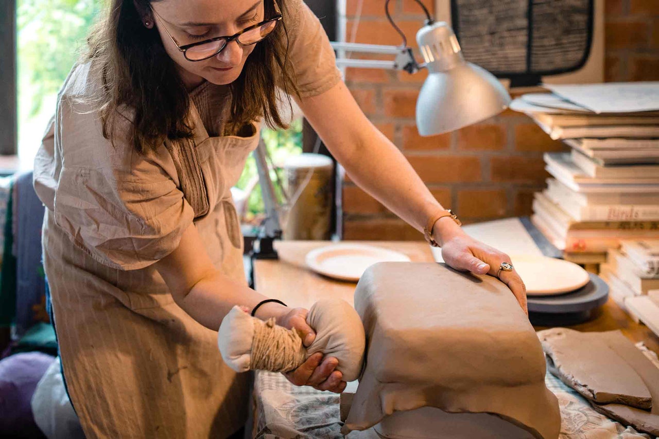 Femeie modelează argila cu unelte într-un atelier.