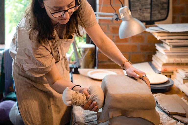 Femeie modelează argila cu unelte într-un atelier.