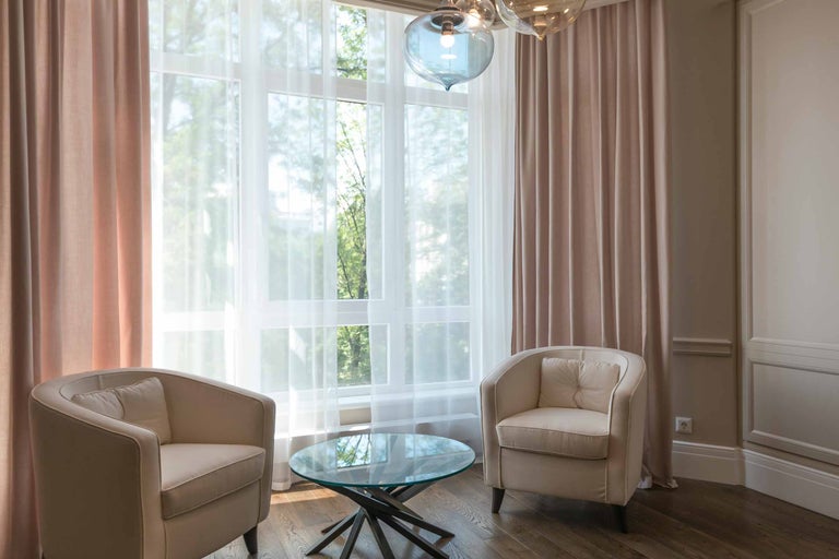 Cameră de zi luminoasă cu fotolii, perdele și masă de sticlă