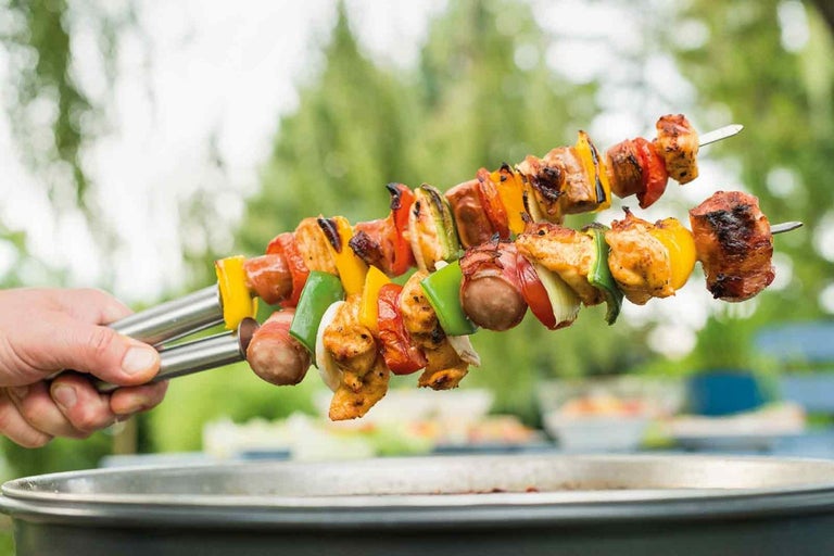 Două frigărui cu carne și legume sunt ținute deasupra unui grătar.