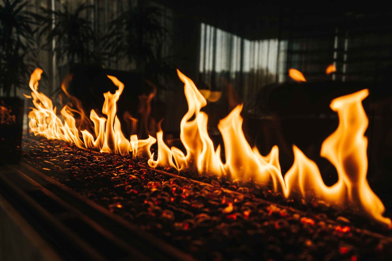 Șemineu modern cu flăcări luminoase peste un pat de pietre decorative incandescente într-un mediu întunecat.