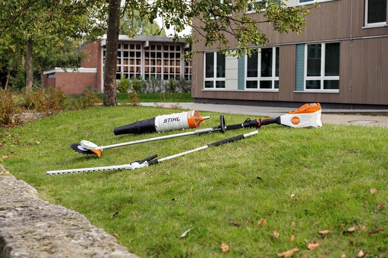 Diverse unelte de grădinărit Stihl sunt așezate pe o zonă cu gazon.