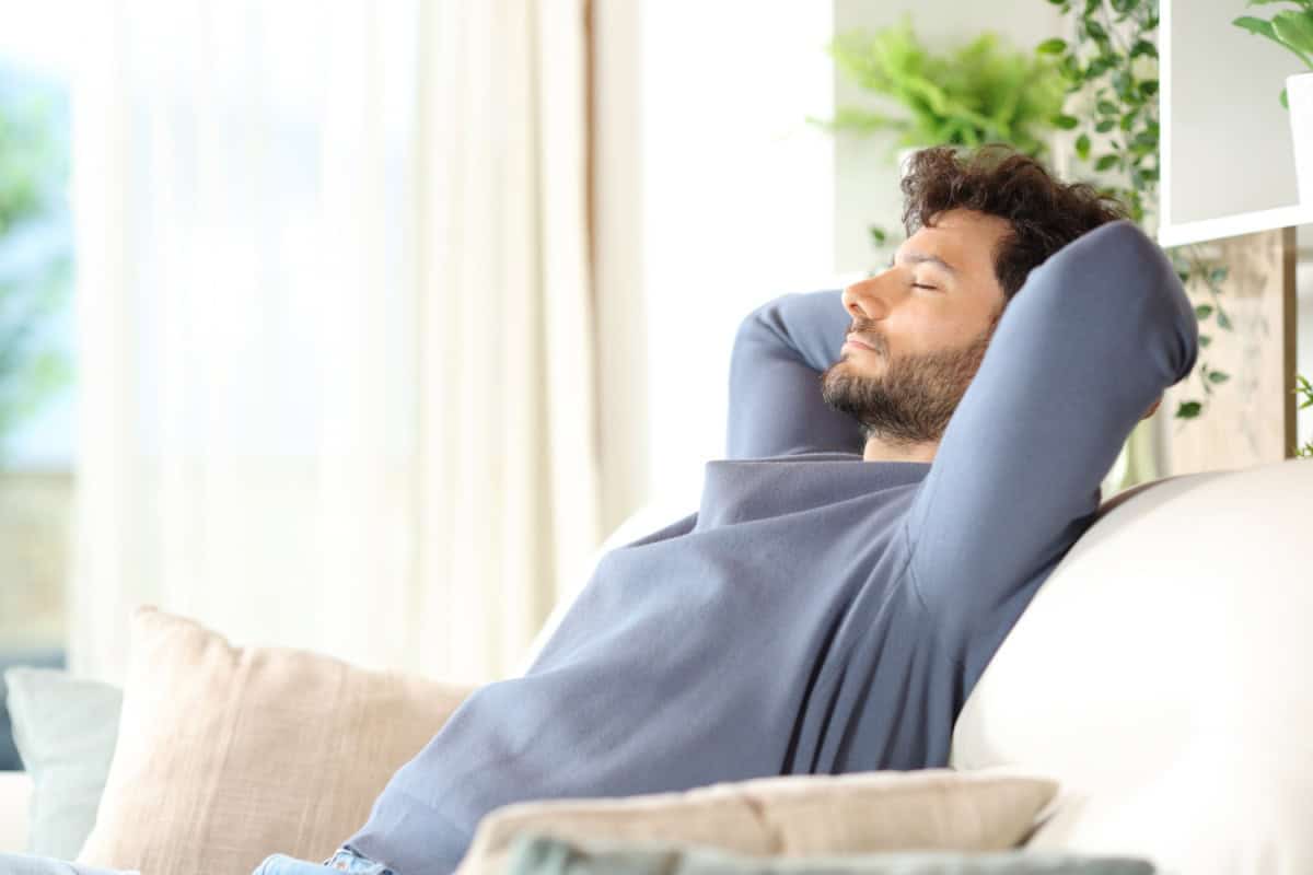 Bărbat relaxându-se pe o canapea într-o sufragerie luminoasă și confortabilă.